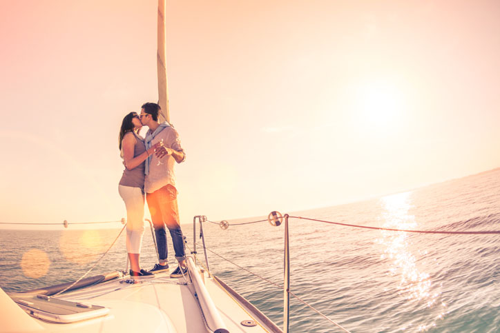 Rich young couple in love on sailboat kissing at sunset